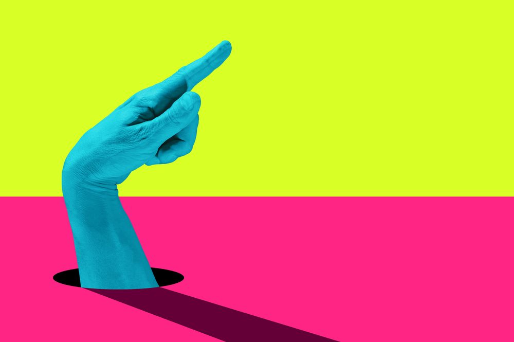 Turquoise hand is pointing to right side, stuck in a yellow and pink background